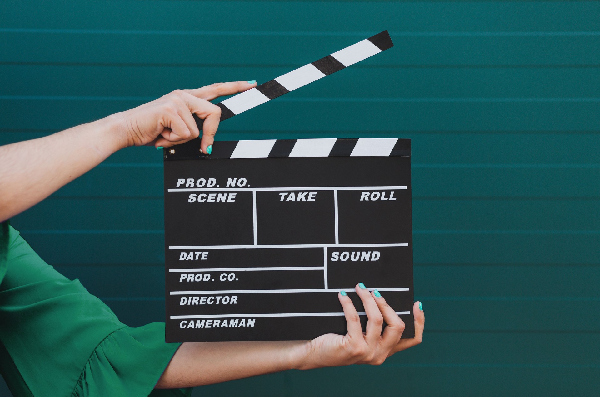 Movie production clapper board holding by female hands against green background.